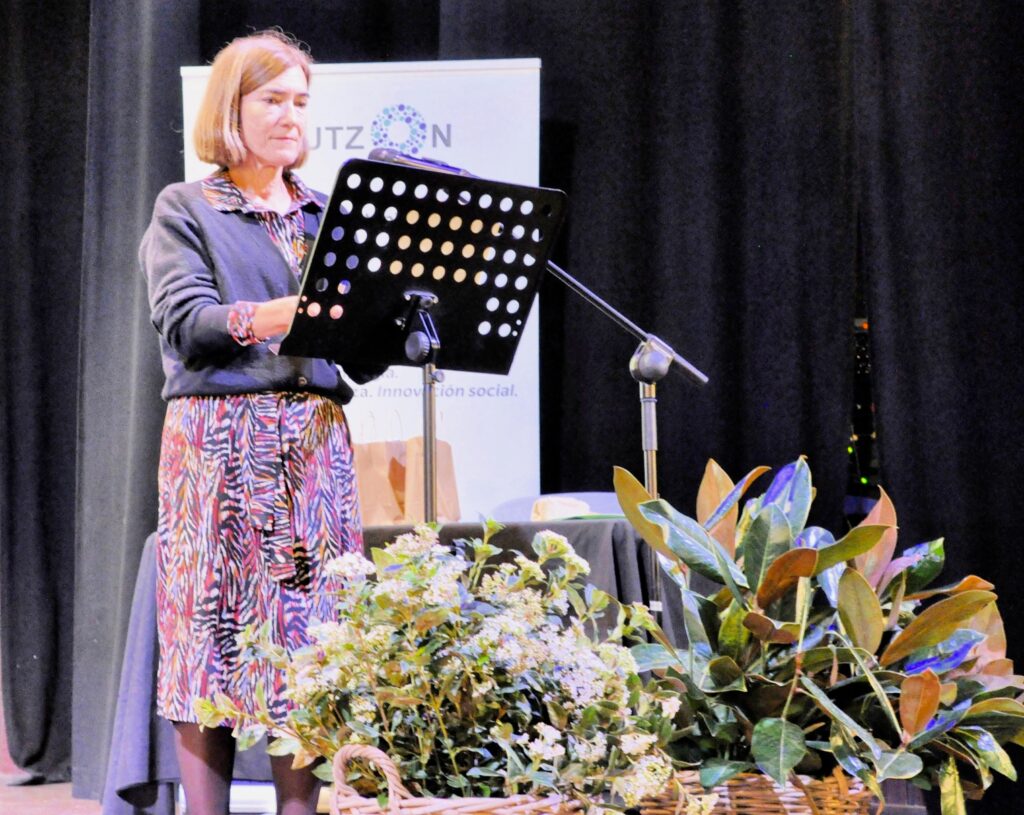 Presentadora en el atril del escenario, junto a unas plantas