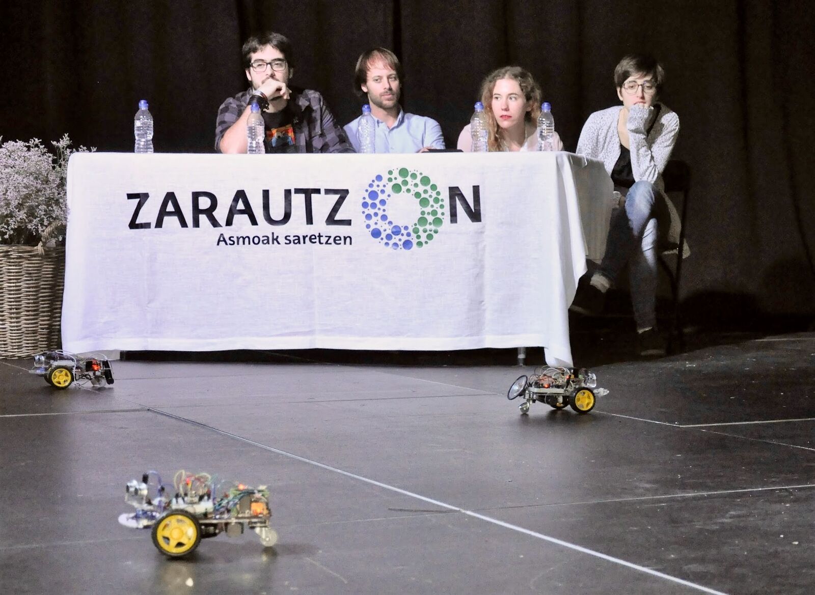 Mesa de ponentes, con dos robots sobre el escenario